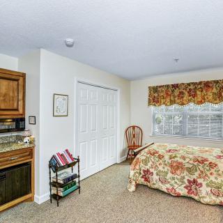 A cozy bedroom featuring floral bedding, a wooden cabinet, and a window with patterned curtains.