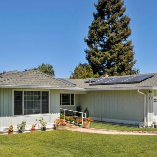 A single-story house with solar panels on its roof, surrounded by a well-maintained lawn and trees on a sunny day.