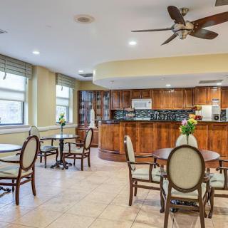 A cozy dining area with wooden cabinets, tables, and chairs, complemented by a ceiling fan and floral decorations.