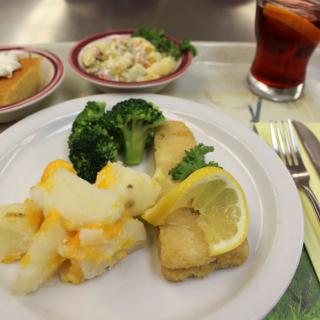 A meal featuring fish with lemon, broccoli, and potatoes, accompanied by coleslaw and a drink.