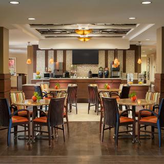 A modern restaurant interior with neatly arranged tables and chairs, featuring a bar counter in the background.
