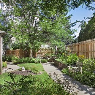 A serene garden with a winding pathway, surrounded by lush greenery and enclosed by a wooden fence.