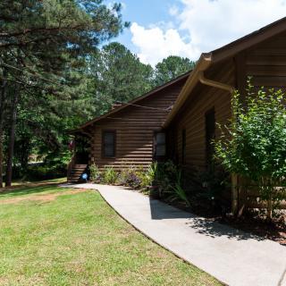 A wooden cabin surrounded by trees and greenery on a sunny day.