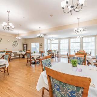 A spacious, well-lit dining room with multiple tables and chairs, adorned with elegant chandeliers and large windows.