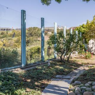A serene garden with a pathway bordered by plants and a fence overlooking a scenic view.
