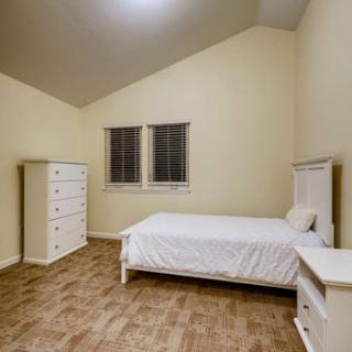 A spacious and minimalist bedroom featuring a single bed, nightstand, and dresser against a light-colored wall.