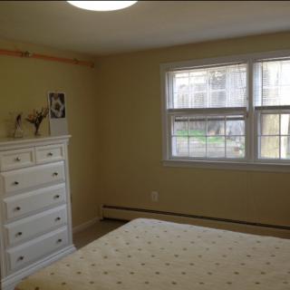 A simple bedroom with a white dresser, bed, and a window letting in natural light.