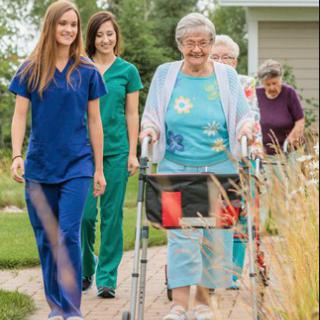 Elderly individuals walking outdoors with the assistance of nurses.