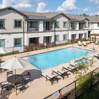 A modern apartment complex featuring an outdoor swimming pool with lounge chairs and umbrellas on a sunny day.
