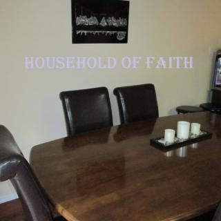 A dining room with a wooden table, chairs, and decorative candles, featuring wall art titled 'Household of Faith'.