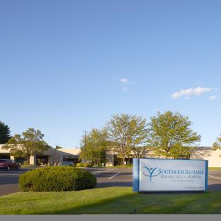 A view of a building with a sign in front, surrounded by trees and grass under a clear sky.