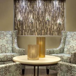 A cozy living room setting featuring two patterned chairs, a round table with decorative lamps, and artistic wall decor.