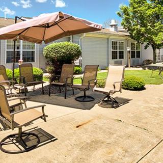 A sunny backyard patio with chairs and an umbrella, surrounded by greenery.