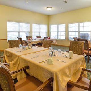 A dining room with tables and chairs set for a meal, illuminated by natural light from large windows.