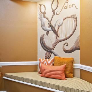A cozy salon waiting area featuring a bench with cushions and decorative scissors artwork on the wall.