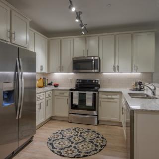 A modern kitchen featuring stainless steel appliances, white cabinets, and a decorative rug.