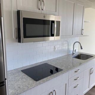 A modern kitchen setup with a microwave, stovetop, sink, and white cabinets.