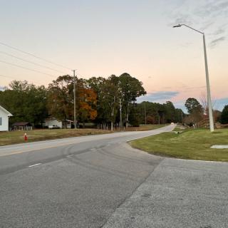 A quiet suburban street at dusk with a lamp post and trees lining the road.