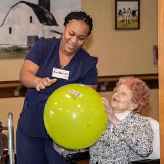 A caregiver engages with an elderly resident, bringing joy through playful interaction with a green ball.