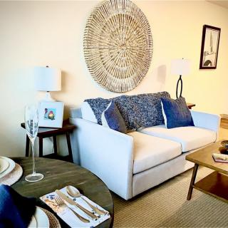 A cozy living room with a white sofa accented by blue pillows, featuring decorative wall art and modern furnishings.