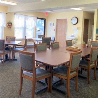 A spacious dining area with multiple tables and chairs, featuring large windows and a carpeted floor.