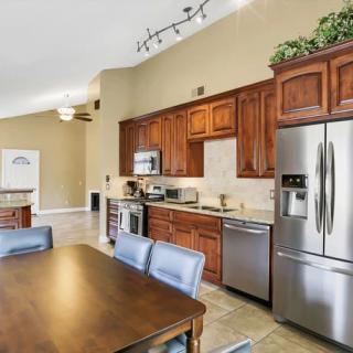 A modern kitchen with wood cabinetry and stainless steel appliances, featuring a dining area with a wooden table and chairs.