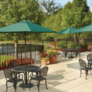A scenic outdoor patio area with tables, chairs, and green umbrellas overlooking a pond.