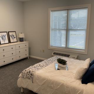 A minimalist bedroom with a neatly made bed, dresser, and a window with blinds.
