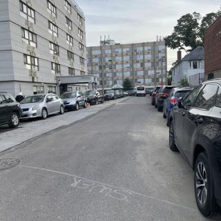 A residential street lined with parked cars and apartment buildings during the day.