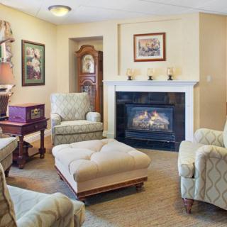 A cozy living room with a fireplace, armchairs, and an ottoman, featuring traditional decor and framed artwork.