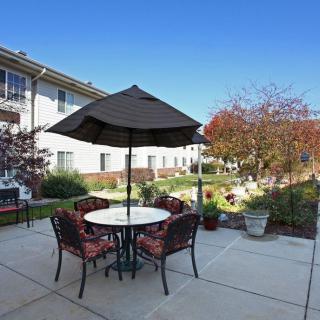 A serene patio setting with a table, chairs, and an umbrella overlooking a garden on a sunny day.