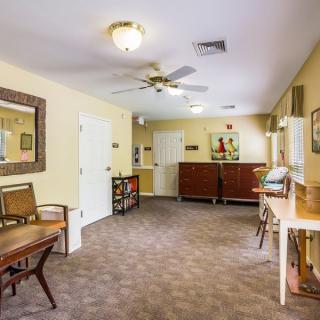 A cozy living room with carpeted flooring, featuring comfortable furniture and decorative elements such as a mirror and artwork on the walls.