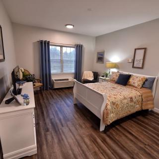 A cozy and well-decorated bedroom with a bed, bedside lamp, and large window.