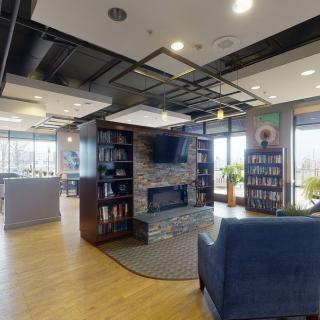 A cozy lounge area with a fireplace, bookshelves, and modern seating.