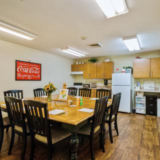 A cozy dining area with a kitchen setup, featuring a large wooden table surrounded by chairs, and equipped with modern appliances and decor.