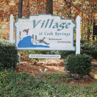 Sign for Village at Cook Springs surrounded by autumn foliage.