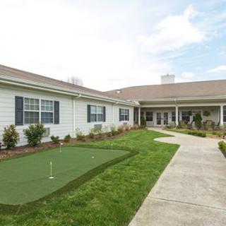 A single-story building with a pathway and putting green in front, under a partly cloudy sky.