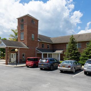 A brick building with a tower, surrounded by a parking lot and trees under a cloudy sky.