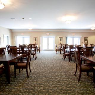 A spacious and well-lit dining room featuring multiple wooden tables and chairs, designed for communal dining.