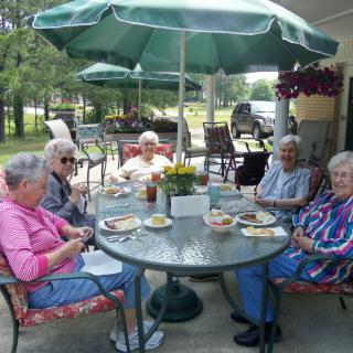 A group of seniors enjoying a meal together on a patio under a large umbrella.