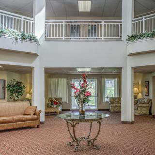 A spacious lobby with a central table displaying flowers, surrounded by comfortable seating and decorated with plants.