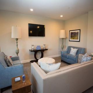 A cozy living room with sofas, a wall-mounted television, and decorative lamps.