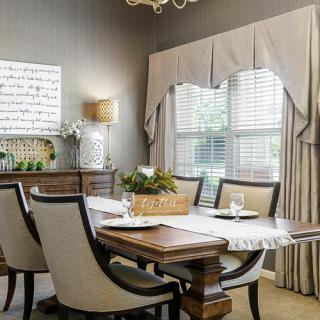 A stylish dining room with an elegant table and chairs, featuring a large window with drapes.