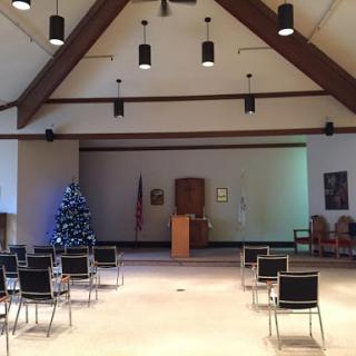 A spacious meeting room decorated with a Christmas tree, featuring rows of chairs and wooden architectural elements.