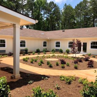 A well-landscaped courtyard features a variety of plants surrounded by a circular pathway, adjacent to a single-story building.