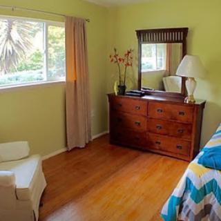 A cozy bedroom featuring a wooden dresser, mirror, and natural light coming through the window.
