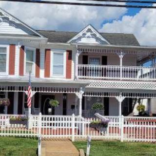 A charming Victorian-style house with a wide porch and white picket fence, set against a partly cloudy sky.
