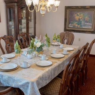 A formal dining room featuring an elegantly set table with dinnerware and a flower arrangement under a chandelier.