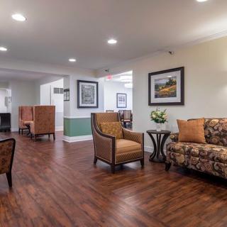 A well-lit lobby area featuring comfortable seating with a sofa and armchairs, complemented by wooden flooring and decorative artwork.