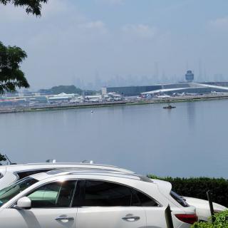 A scenic view of cars parked near a waterfront with modern architecture in the background.